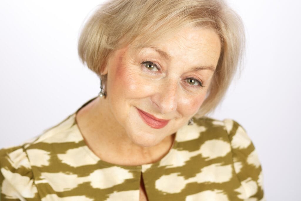 Headshot of middle aged lady with short blond hair and beige dress on our about you studio page