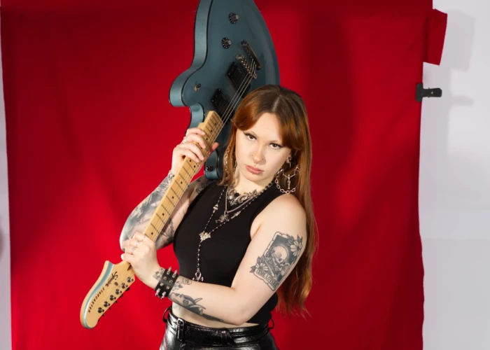 Tattooed young lady with red hair on a red background holding a guitar in the air